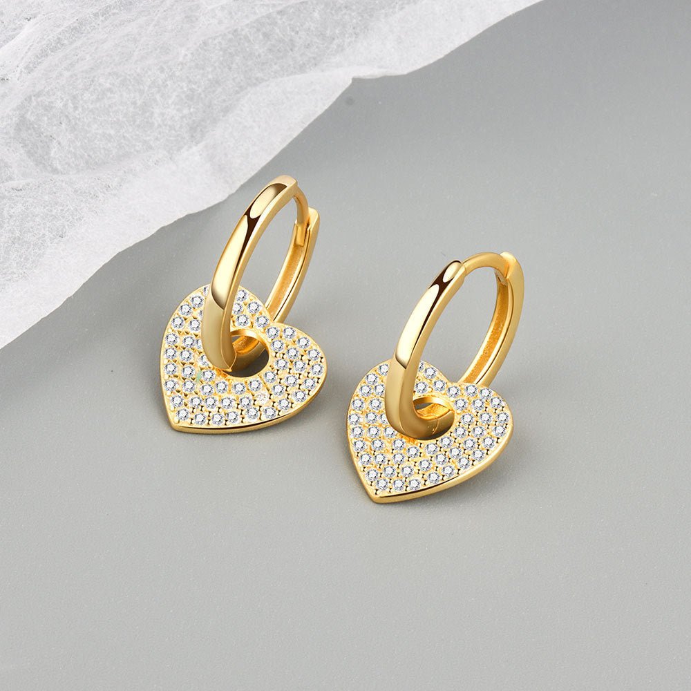 Gold heart-shaped earrings with embedded stones on a gray surface