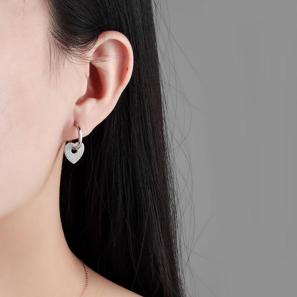 Heart-shaped earring worn by a person with a neutral background