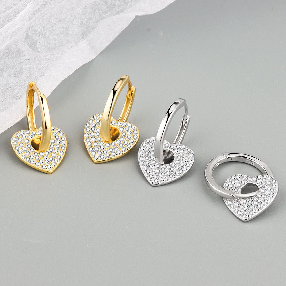 Heart-shaped earrings in gold, silver, and a keychain in silver on a light gray background.