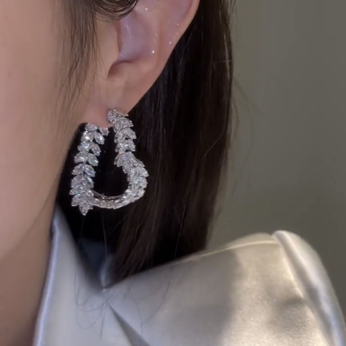 Close-up of a person wearing sparkling silver hoop earrings with a neutral background.