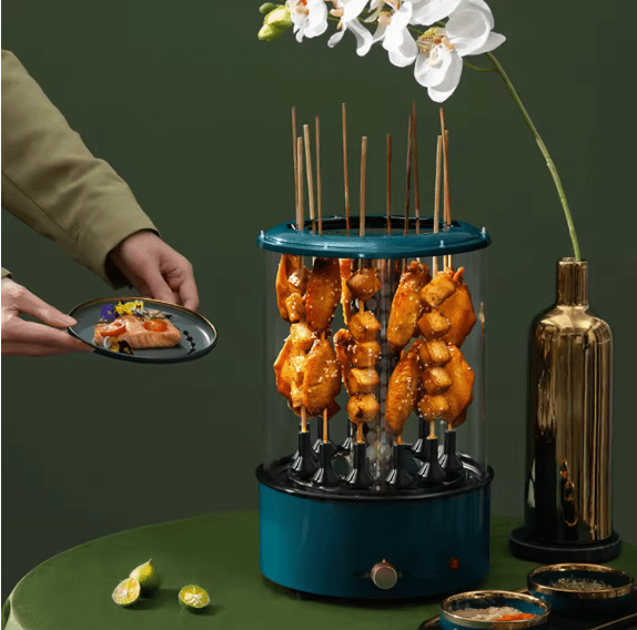 Blue skewer holder with grilled food on a green surface, with a person holding a plate of food.