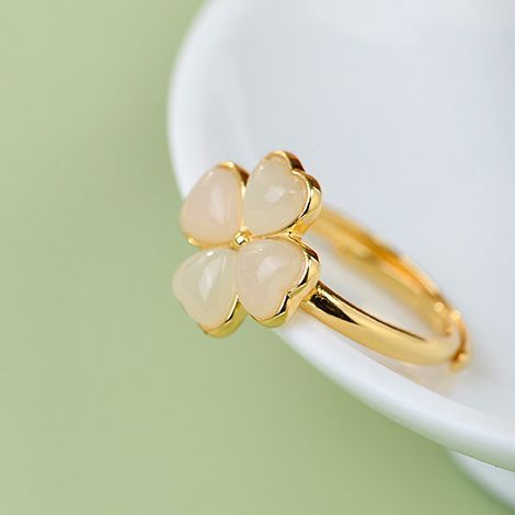 Gold ring with three heart-shaped stones on a white surface with a green background