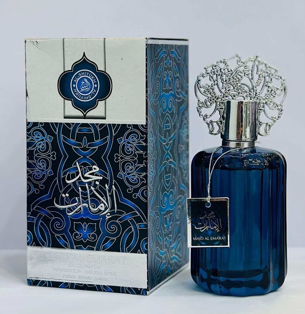 Blue perfume bottle with intricate design and decorative box on a light gray background