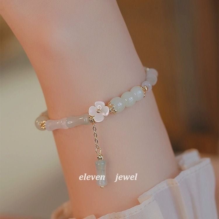 Delicate bracelet with floral charm and gemstone on a wrist, branded 'eleven jewel'.