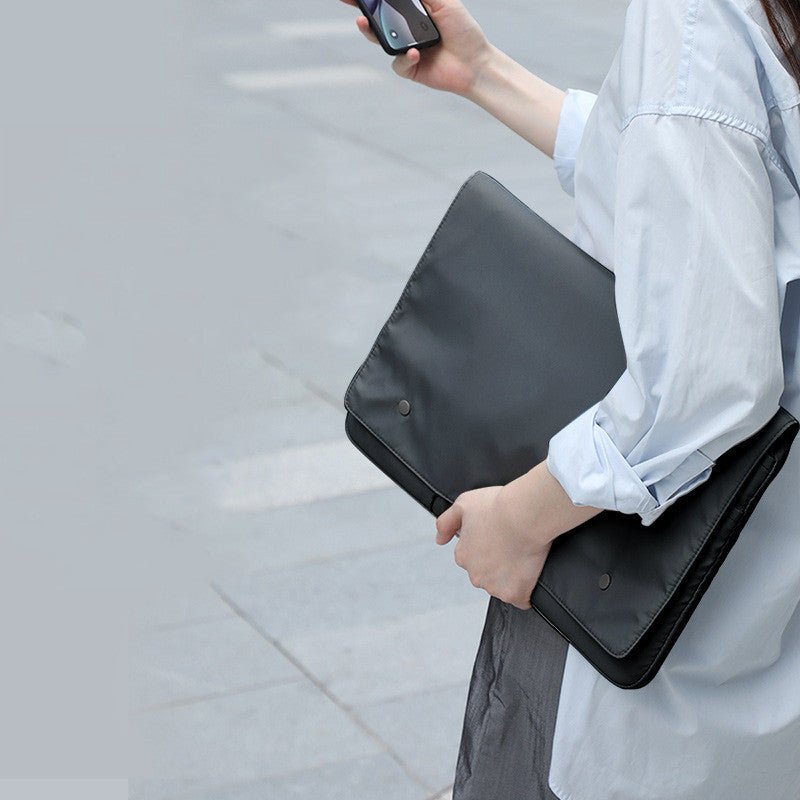 Person holding a black laptop case on a light gray pavement background