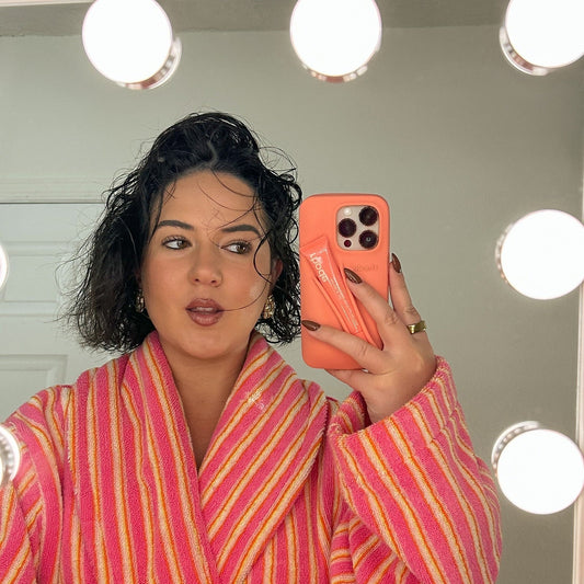 Person wearing a pink and orange striped robe taking a mirror selfie with a phone.