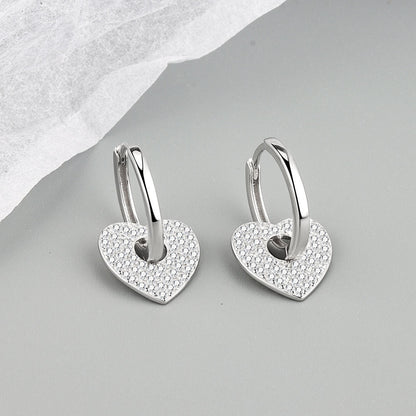 Heart-shaped silver earrings with embedded stones on a gray surface
