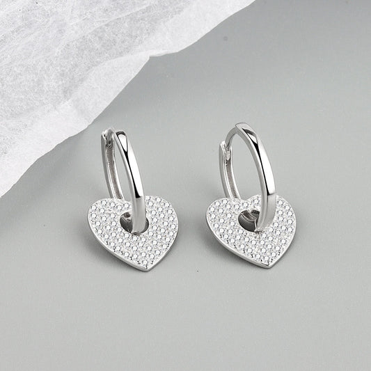 Heart-shaped silver earrings with embedded stones on a gray surface