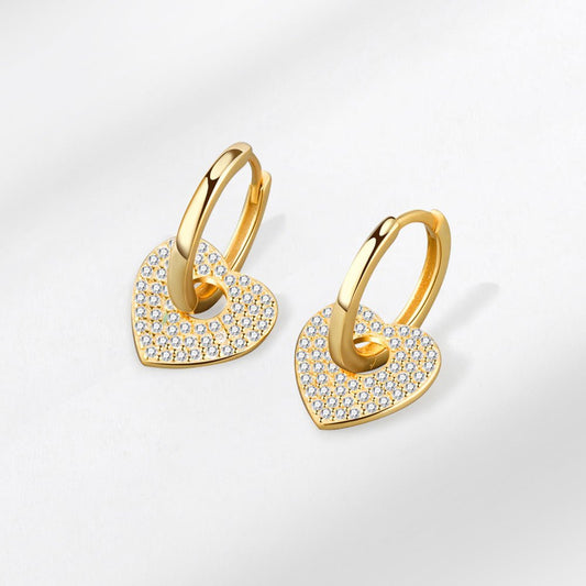 Gold heart-shaped earrings with embedded stones on a light gray background