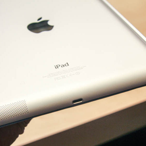 Close-up of an Apple iPad held by a hand on a wooden surface