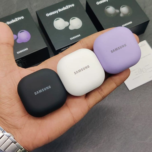 Hand holding three Samsung Galaxy Buds Pro in black, white, and purple with product boxes in the background.