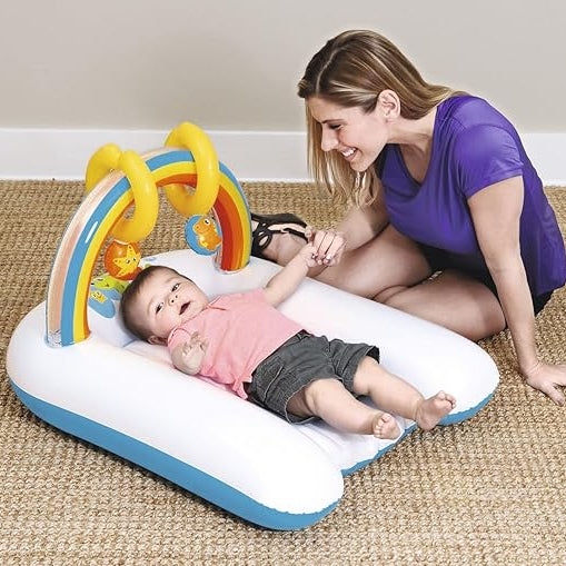Baby lying on an inflatable play mat with a rainbow arch, being played with by a woman.