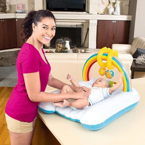 Woman playing with a baby on an inflatable play mat with rainbow design in a living room.