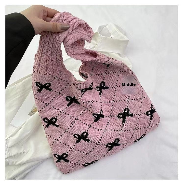 Pink knitted bag with black patterns held by a hand on a white background