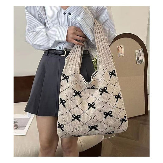 Person holding a beige tote bag with black bow pattern in an indoor setting