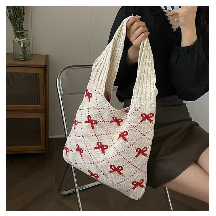 Person holding a white knitted bag with red patterns in an indoor setting