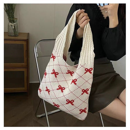 Person holding a white knitted bag with red patterns in an indoor setting