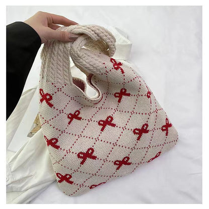 Knitted bag with red patterns held by a hand on a white background