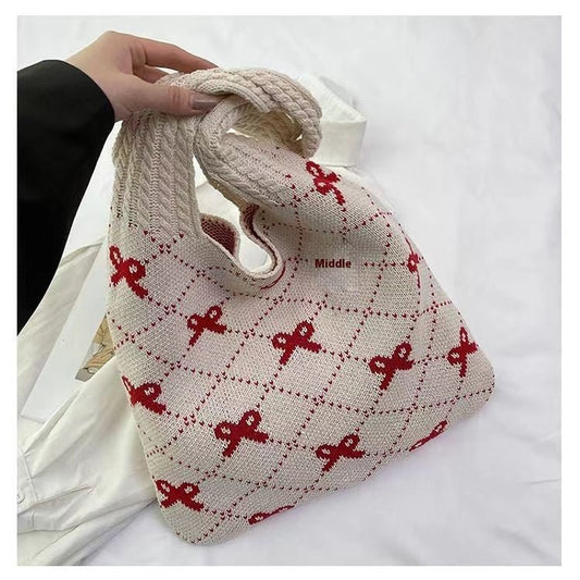 Knitted bag with red patterns held by a hand on a white background