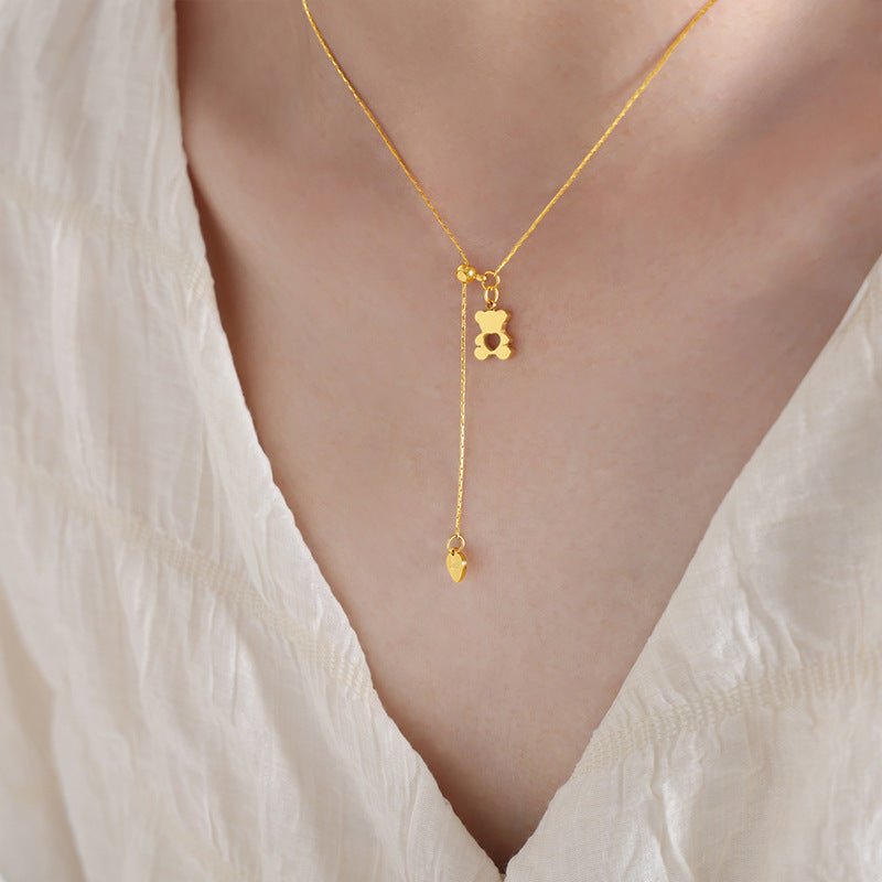 Gold necklace with a teddy bear pendant on a person wearing a white top.