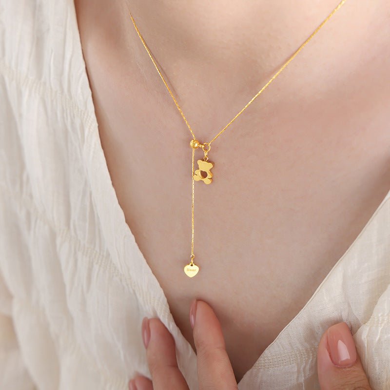 Gold necklace with a teddy bear pendant worn by a person against a white background