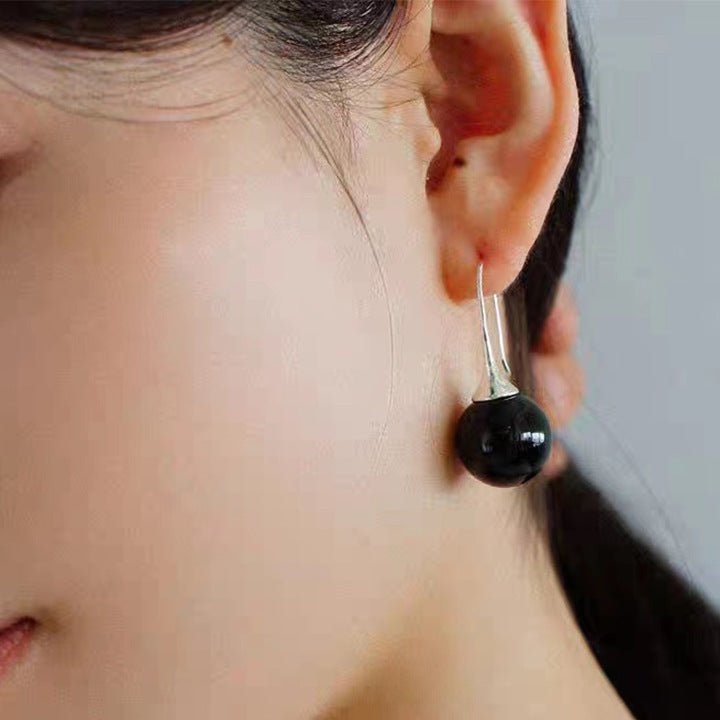 Close-up of a person wearing a black earring with a silver setting.