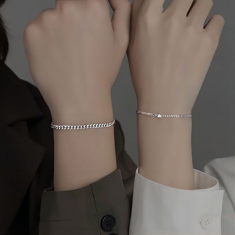 Two wrists wearing silver chain bracelets against a neutral background