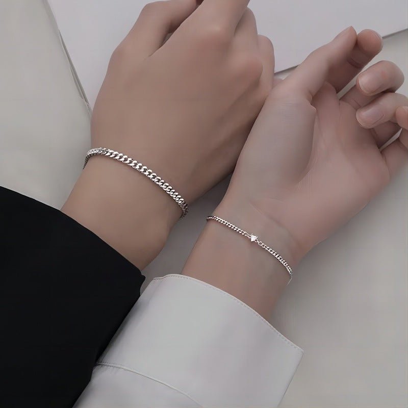 Two wrists wearing silver bracelets on a neutral background