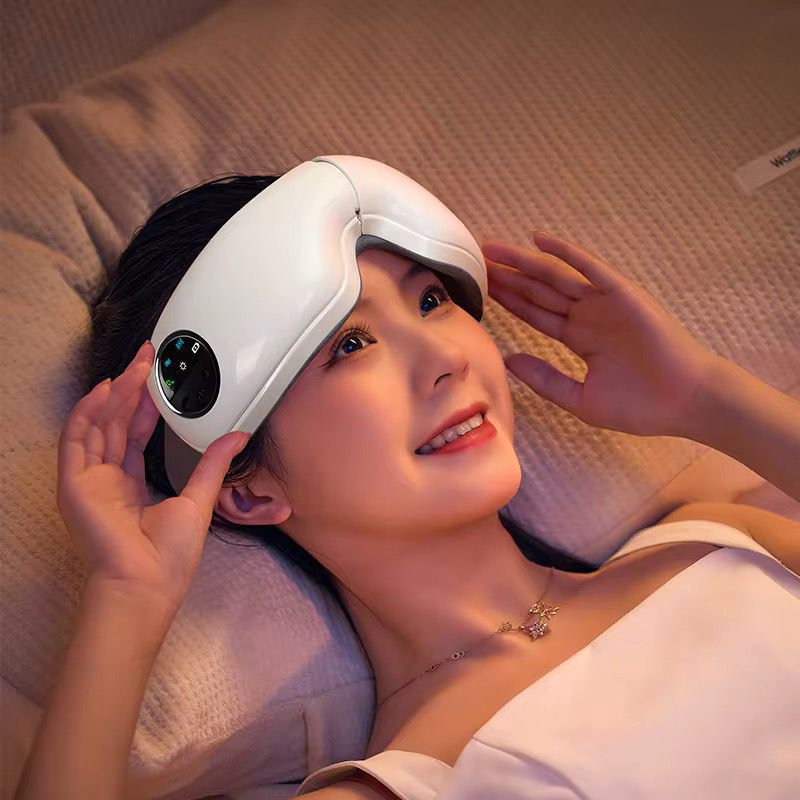 Woman using a white eye massager on a beige blanket