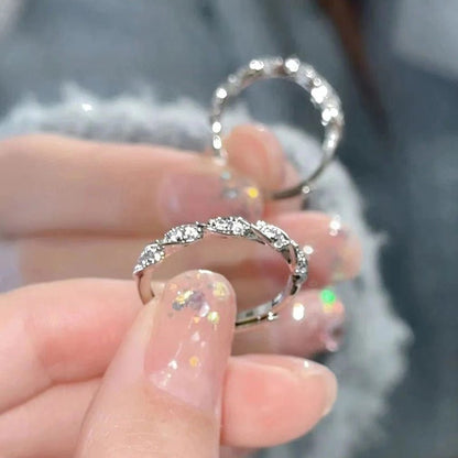 Silver ring with gemstones held between fingers against a blurred background