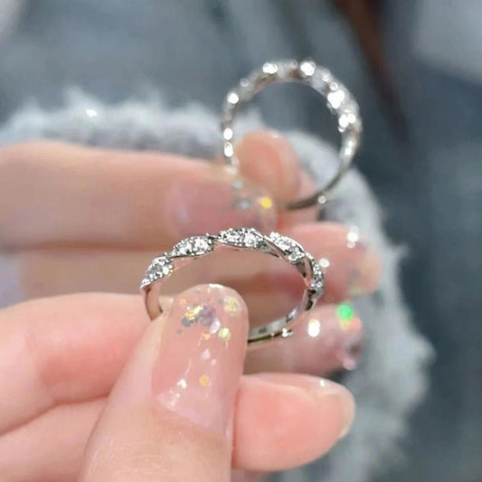 Silver ring with gemstones held between fingers against a blurred background