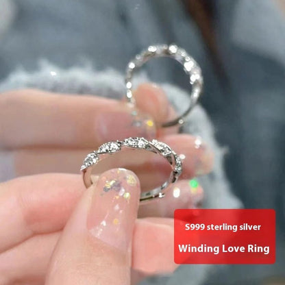 S999 sterling silver winding love ring held in a hand with a blurred background