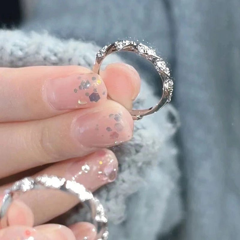 Silver ring held by a hand with glittery nail polish against a blurred background