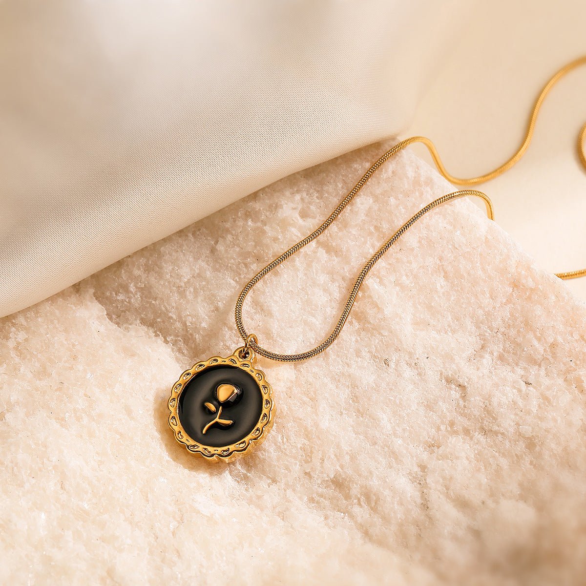 Gold necklace with a black pendant featuring a rose design on a beige fabric background