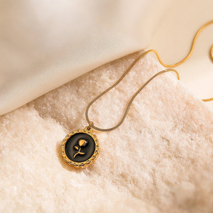 Gold necklace with a black pendant featuring a rose design on a beige fabric background