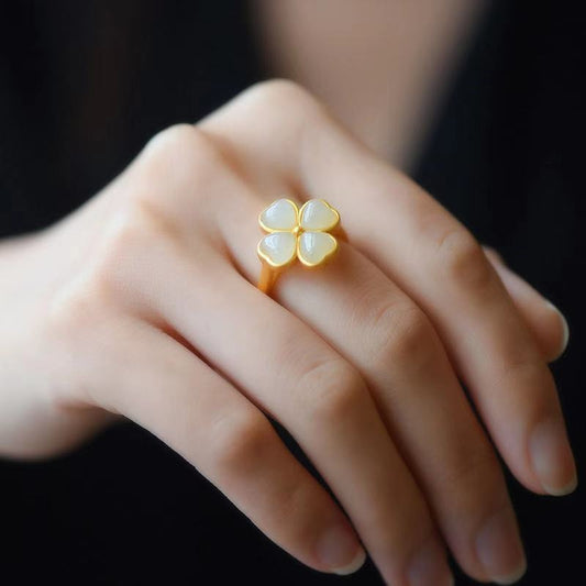 Gold ring with a four-leaf clover design on a person's finger against a dark background