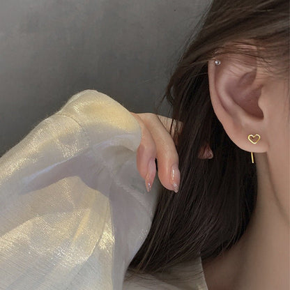 Close-up of an ear wearing a heart-shaped earring with a neutral background