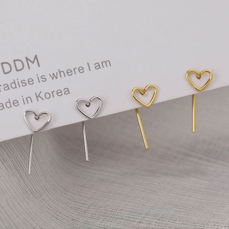 Heart-shaped earrings in gold and silver on a textured surface with text in the background.