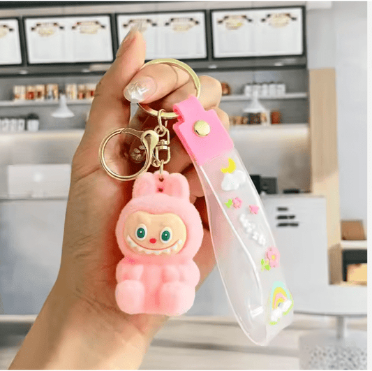 Hand holding a pink labubu keychain with a character design in an indoor setting