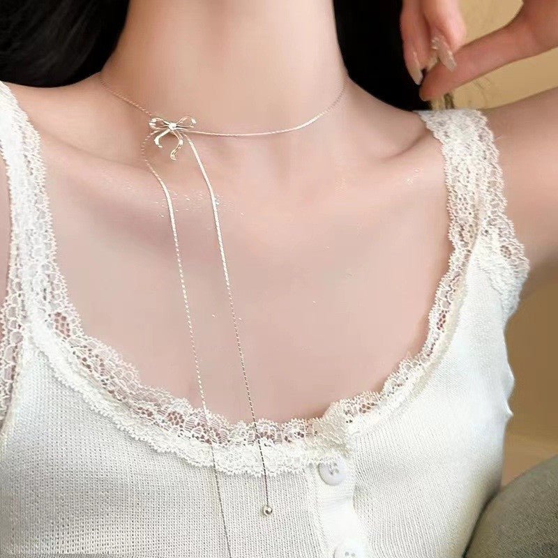 Close-up of a person wearing a delicate necklace with a bow pendant.