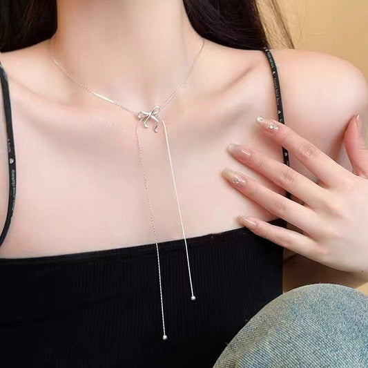 Woman wearing a black strappy top with a long necklace, hand touching chest.