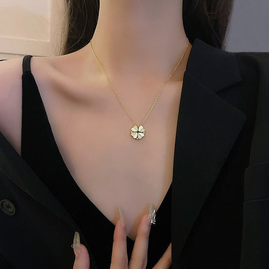 Gold necklace with a clover pendant worn by a person in a black outfit.