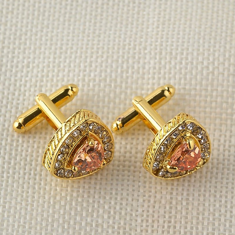 Gold cufflinks with pink gemstones on a textured beige background