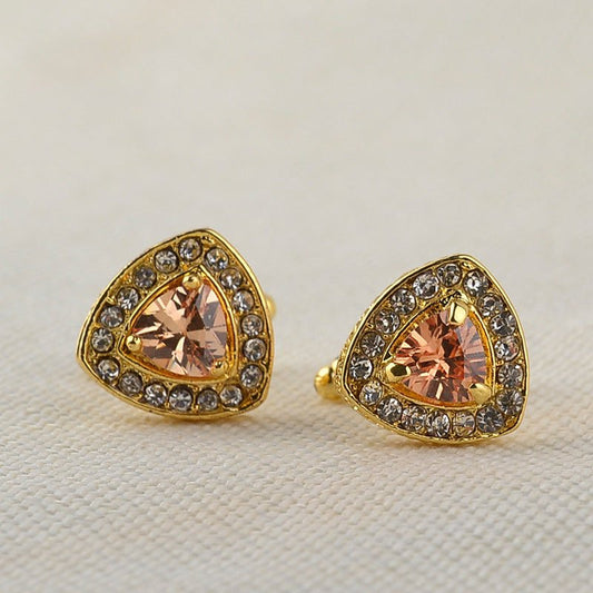 Pair of gold-trimmed earrings with peach-colored gemstones on a light background