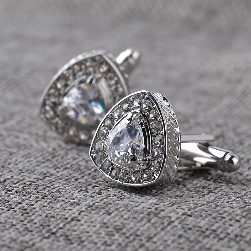 Silver cufflinks with clear gemstones on a textured gray surface