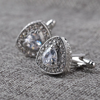 Silver cufflinks with clear gemstones on a textured gray surface