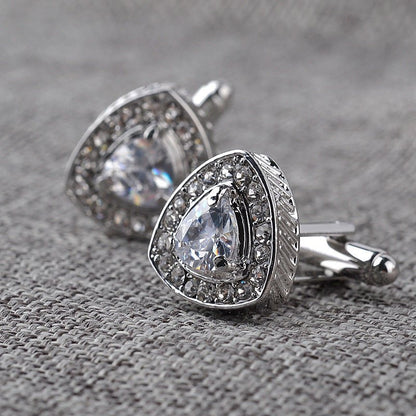 Silver cufflinks with clear gemstones on a textured gray surface