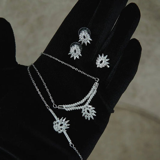 Silver jewelry set with necklace and earrings on a black glove against a neutral background