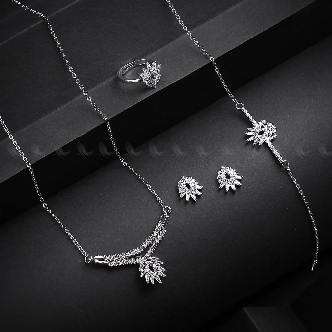 Silver jewelry set including necklace, ring, and earrings on a dark surface.
