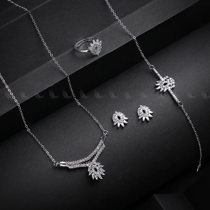 Silver jewelry set including necklace, ring, and earrings on a dark surface.
